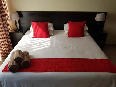 a bed with two red pillows and a red blanket at 360 Eastwoods Guesthouse in Pretoria