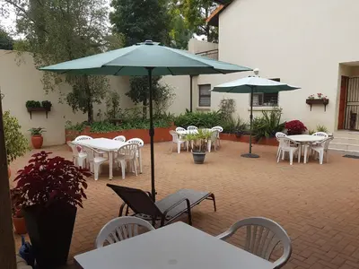 a patio with tables and chairs and an umbrella at 360 Eastwoods Guesthouse in Pretoria