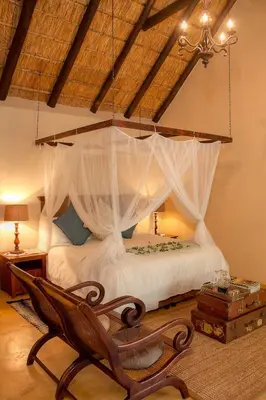 a bedroom with a canopy bed with a chair at Mvuradona Safari Lodge in Marloth Park