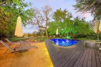 a wooden deck with a pool and chairs and an umbrella at Mvuradona Safari Lodge in Marloth Park