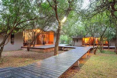 a wooden bench in front of a house with trees at Mvuradona Safari Lodge in Marloth Park