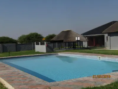 a large blue swimming pool with a thatched building at Vido Lodge and Conference Centre in Polokwane