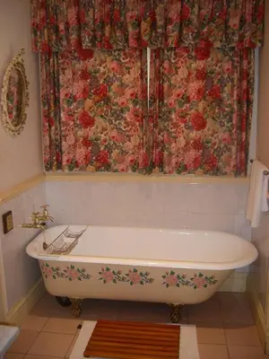 a bath tub in a bathroom with a floral shower curtain at Sherwood's Country House in Tzaneen