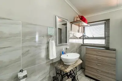 a white bathroom with a sink and a mirror at Berghaan Pretoria in Pretoria