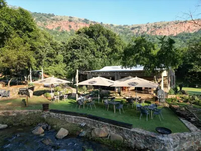 a restaurant with tables and umbrellas next to a river at Rocky Drift Private Nature Reserve in Waterval Boven