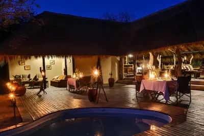a patio with a table and a swimming pool at night at Tangala Safari Camp in Thornybush Game Reserve