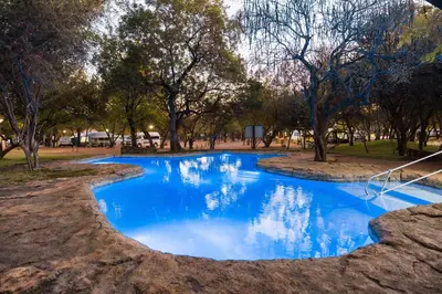 a pool of blue water in a park with trees at Phalaborwa Safari Park, A Forever Resort in Phalaborwa