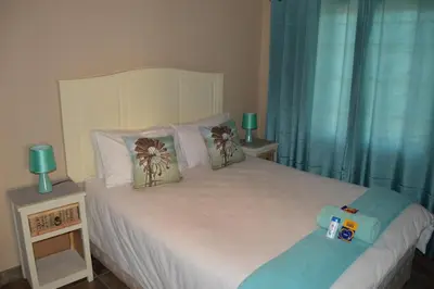 a bedroom with a white bed with blue curtains at Esmarline Lodge in Brits