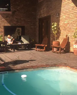 a swimming pool with chairs and a person sitting on a patio at Hakuna Matata in Marloth Park