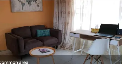 a living room with a couch and a desk with a laptop at LANGA 'S COZY GUESTHOUSE in Pretoria