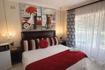 a bedroom with a red bed with a painting on the wall at La Barune Guest House in Tzaneen