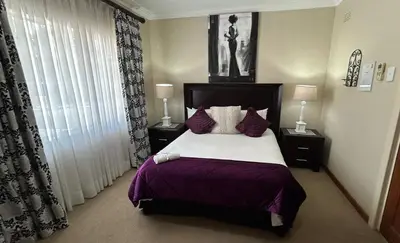 a bedroom with a large bed with purple sheets and pillows at La Barune Guest House in Tzaneen