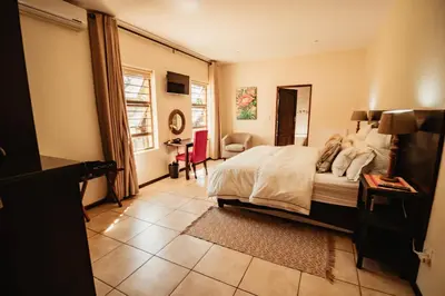 a bedroom with a bed and a chair and a table at Blue Hills Lodge in Midrand