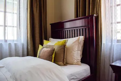a bed with white sheets and pillows next to a window at Ambassador Lodge in Dullstroom