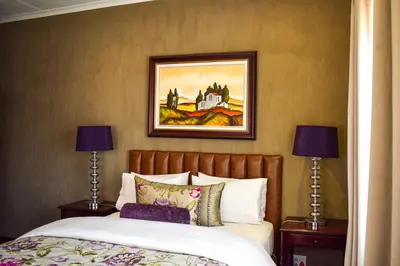 a bedroom with a bed with a painting on the wall at Ambassador Lodge in Dullstroom