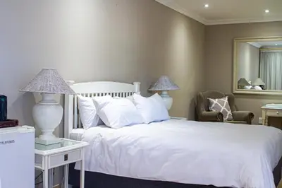 a bedroom with a white bed and a chair and a mirror at Machauka Lodge in Lephalale