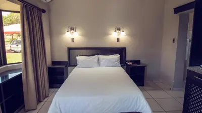 a bedroom with a bed with white sheets and a window at Machauka Lodge in Lephalale