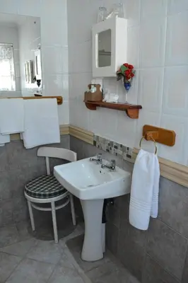 a bathroom with a sink and a chair and a mirror at Le Chateau Guest House and Conference Centre in Kempton Park