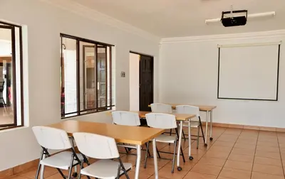 a classroom with tables and white chairs and a whiteboard at Indlovukazi Guesthouse in Hartbeespoort