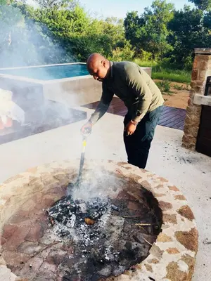 a man standing over a fire in a fire pit at Kuwisa Lodge in Bela-Bela