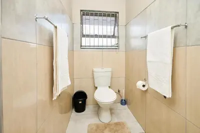 a bathroom with a toilet and a window and towels at Menlyn Maine Spacious Cottage in Pretoria