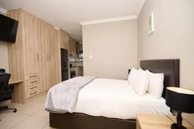 a bedroom with a white bed and a kitchen at Menlyn Maine Spacious Cottage in Pretoria