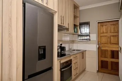 a kitchen with a stainless steel refrigerator and wooden cabinets at Menlyn Maine Spacious Cottage in Pretoria