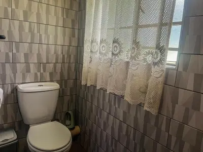a bathroom with a toilet and a window with curtains at Leribisi Lodge in Tierpoort