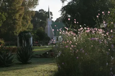 a garden with pink flowers in front of a church at The Highveld Cape Inn in Pretoria