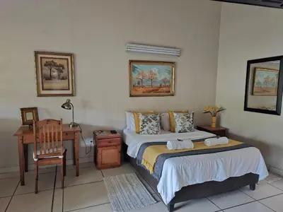 a bedroom with two beds and a desk and a table at Tzaneen White House Lodge in Tzaneen