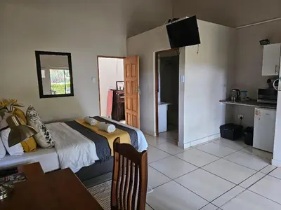 a bedroom with a bed and a table and a kitchen at Tzaneen White House Lodge in Tzaneen