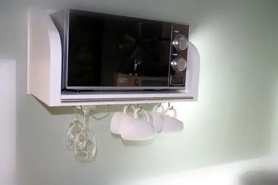 a microwave on a wall with four wine glasses and a rack at Serendipity NO TV in Polokwane
