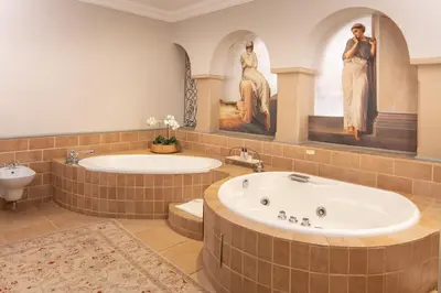 a bathroom with two tubs and two statues of women at Castello Di Monte in Pretoria