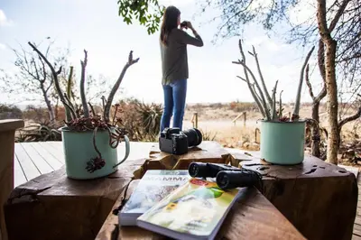 a woman standing on a wooden table with a camera at Klaserie Drift Misava in Klaserie Private Nature Reserve