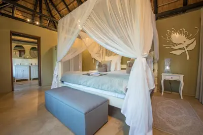 a bedroom with a canopy bed with a blue ottoman at Kambaku Safari Lodge in Timbavati Game Reserve