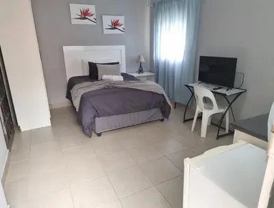 a bedroom with a bed and a desk with a computer at Stay at Home Airport Lodge in Kempton Park