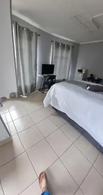 a person standing in a bedroom with a bed and a desk at Stay at Home Airport Lodge in Kempton Park