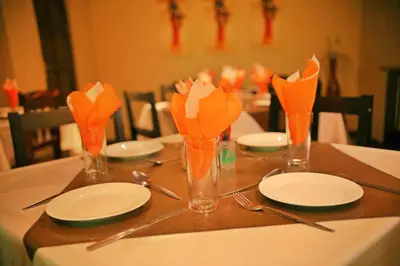a table with white plates and orange flowers in vases at Mmakosha Lodge in Pretoria