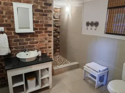 a bathroom with a sink and a brick wall at Arend Cottage in Nelspruit