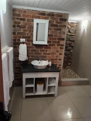 a bathroom with a sink and a brick wall at Arend Cottage in Nelspruit