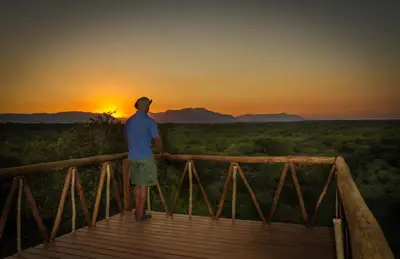 a man standing on a wooden bridge looking at the sunset at Panzi Lodge in Guernsey Nature Reserve