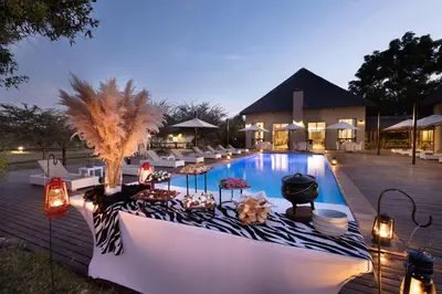 a pool with chairs and umbrellas next to a building at Safari Plains in Mabula