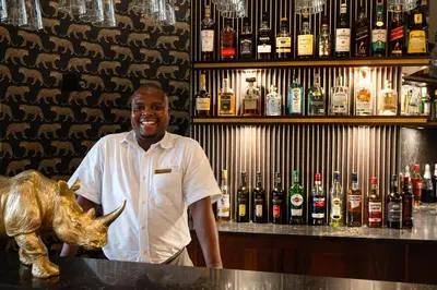 a man standing behind a bar with a rhino statue at Kings Camp in Timbavati Game Reserve