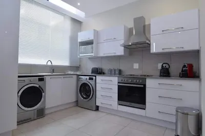 a kitchen with white cabinets and a washer and dryer at Elridge Living in Boksburg