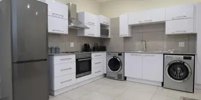 a kitchen with white cabinets and a washer and dryer at Elridge Living in Boksburg