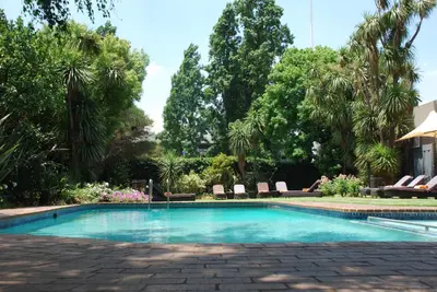 a swimming pool with chairs and palm trees at Southern Sun OR Tambo International Airport in Kempton Park