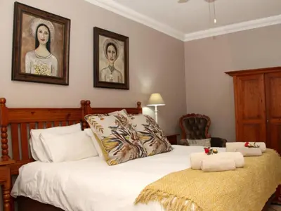 a bedroom with a bed and two portraits on the wall at Feathers Guest House in Middelburg