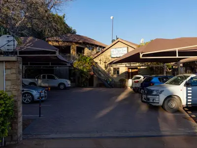 a parking lot with cars parked in front of a building at Palm Inn Guesthouse in Onverwacht