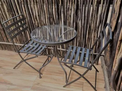 a glass table and two chairs next to a wall at Palm Inn Guesthouse in Onverwacht