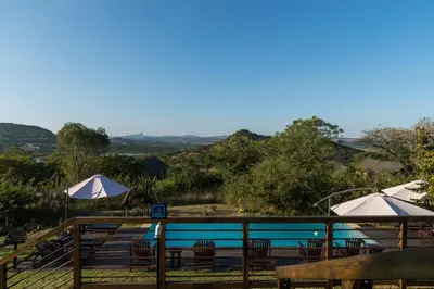 a pool with tables and chairs and umbrellas at Ndhula Luxury Tented Lodge in White River
